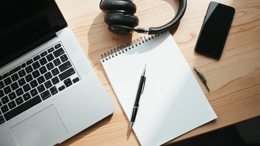 Un ordinateur portable, des écouteurs, un crayon et un cahier vierge sur un bureau en bois.